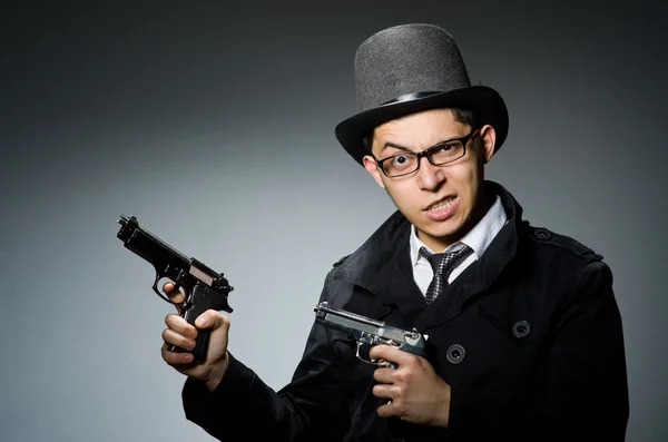 Преступник в черном пальто держит ружье против серого — стоковое фото