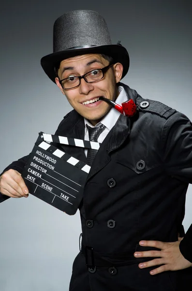 Detective in black coat with clapperboard against gray — Stock Photo, Image