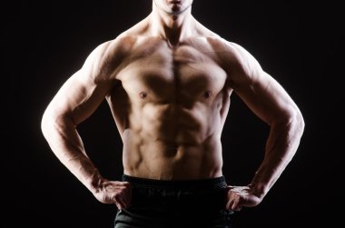 Kaslı adam karanlık stüdyoda poz veriyor.