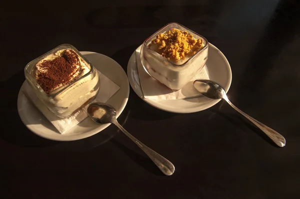 Cheesecake e tiramisu em óculos sobre fundo preto — Fotografia de Stock