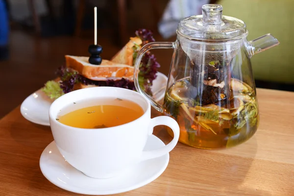 Glass teapot, cup of tea and sandwich on wooden table