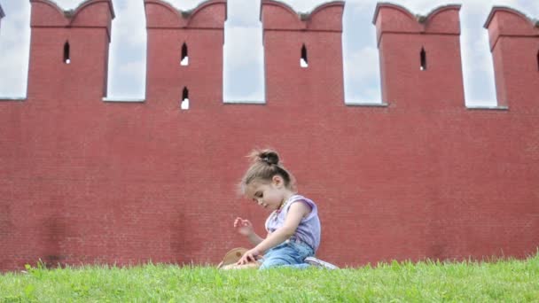 Menina senta-se perto de grande parede vermelha — Vídeo de Stock