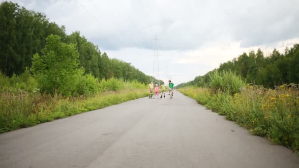 Happy parents faire du vélo et deux enfants patiner à roulettes sur la route 