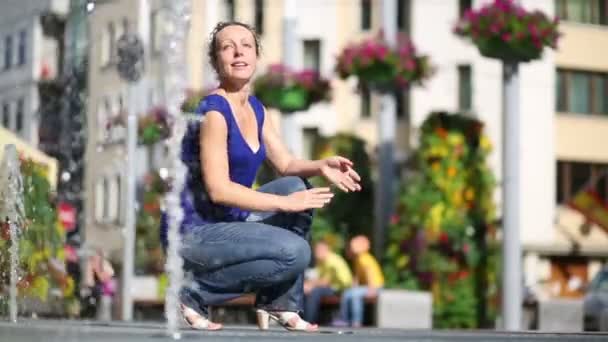 Donna sorridente in vestiti bagnati accovaccia vicino fontana al giorno d'estate — Video Stock