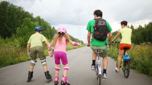 Back of mother and father riding bikes and children rolling skate — Stock Video