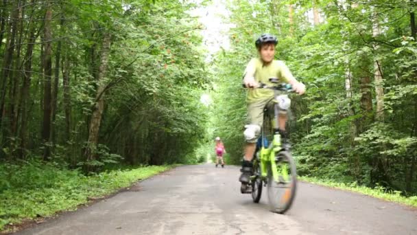 Щасливий хлопчик в шоломі їде на велосипеді по дорозі в літньому парку — стокове відео