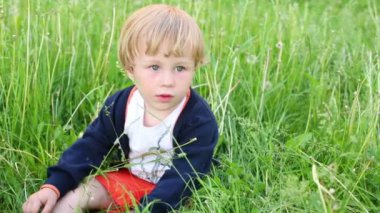 Küçük sarışın çocuk çimenlerin üzerinde oturur