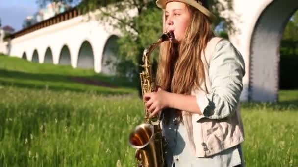 Hermosa chica toca el saxofón cerca del acueducto en verano — Vídeo de stock