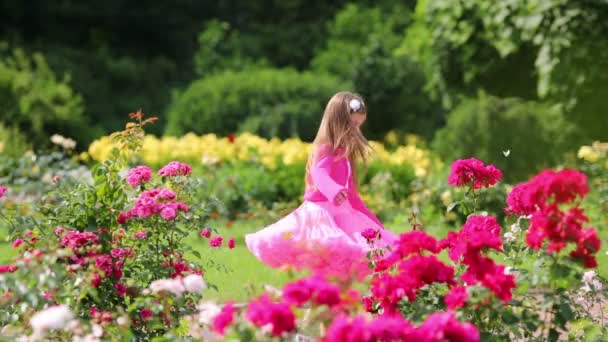 Klein meisje in roze weelderige rok draait en glimlacht onder bloemen — Stockvideo