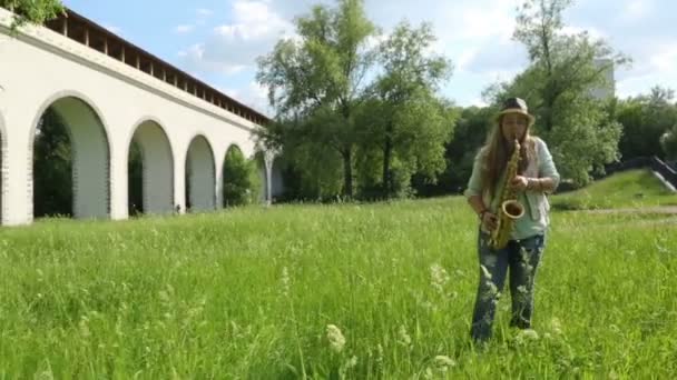 Caminhando menina de chapéu toca saxofone — Vídeo de Stock