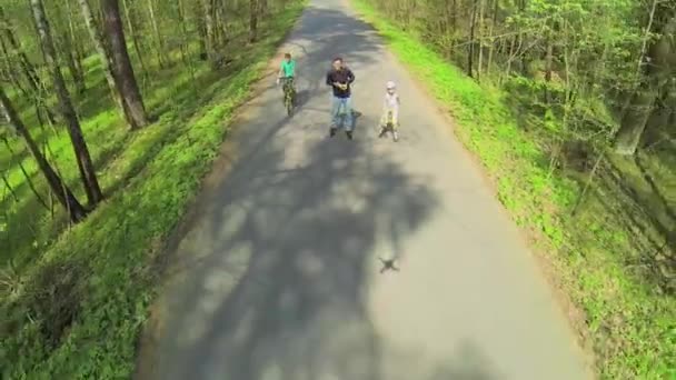 Дети с отцом катаются на роликах и велосипедах — стоковое видео