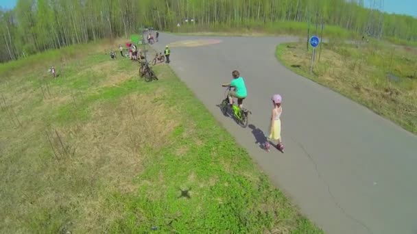Two kids ride on rollerskates and bicycle — Stock Video