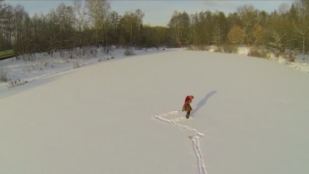 Kvinnan lämnar spår på insnöade dammen — Stockvideo