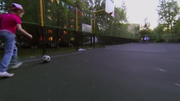 Niña conduce pelota de fútbol por patio de recreo en la noche de primavera — Vídeo de stock