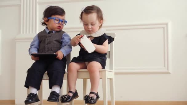 Malý chlapec s tabletovým počítačem sedí vedle dětské holčičky s telefonem — Stock video