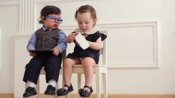 Niño con tableta se sienta al lado de la niña con el teléfono — Vídeo de stock