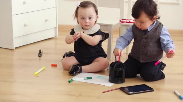 Baby boy and baby girl sit on floor play with colored markers — Stock Video