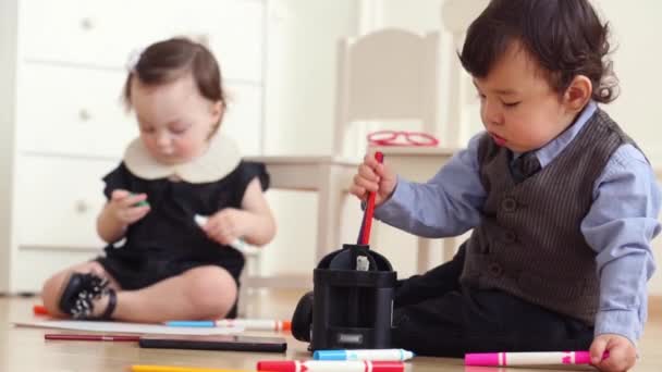 Симпатичные мальчик и девочка сидят на полу, играют с маркерами — стоковое видео
