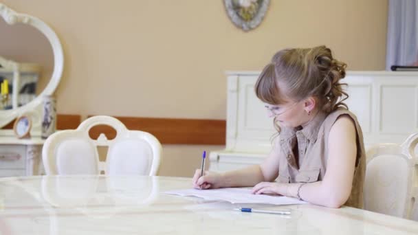 Hermosa chica en gafas se sienta a la mesa y escribe en papel — Vídeos de Stock