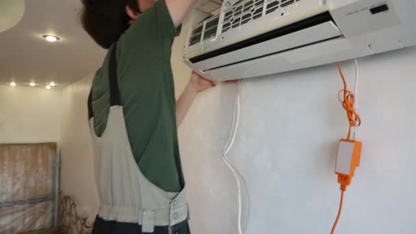 Человек в рабочей одежде демонтирует кондиционер в помещении — стоковое видео