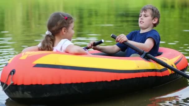 Garçon et fille tirent hors de la rive de l'étang dans le bateau gonflable . — Video