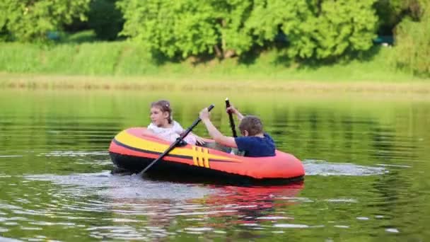 Niño y niña flotan en bote inflable con remos en estanque . — Vídeo de stock