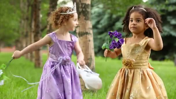Dos niñas con hermosos vestidos sostienen flores en el parque — Vídeos de Stock