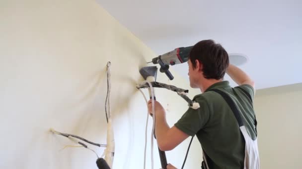 El hombre está perforando el agujero en la pared y elimina el polvo con la aspiradora — Vídeos de Stock