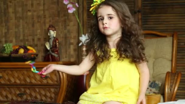 Little curly girl in yellow dress is shaking bracelet . — Stock Video