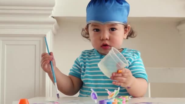 Baby jongen in blauwe afstuderen drankjes aan tafel met inkten — Stockvideo