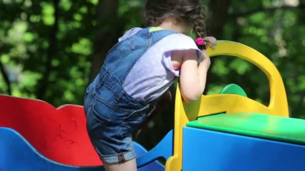 Menina bonito em macacões está jogando em um carro colorido . — Vídeo de Stock