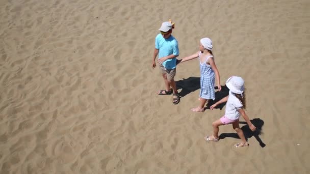 Tres niños felices juegan al ciego en la arena amarilla de la playa — Vídeo de stock