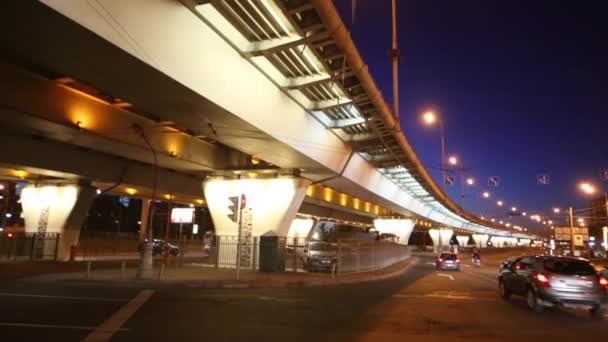 Achterkant van veel auto's die op de weg in de buurt van viaduct 's nachts bewegen — Stockvideo