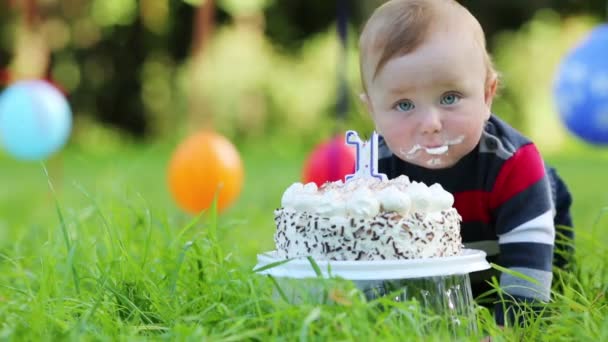 Cute baby eats cake with candle in form of 1 at summer park — Stock Video