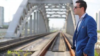Young man in sunglasses looks at wristwatch on railway bridge