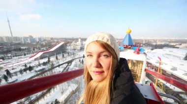 Young pretty woman smiles and looks at sun on ferris wheel