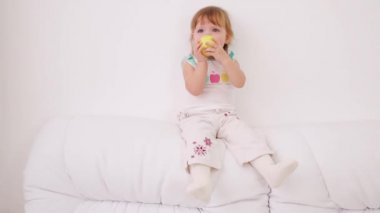 Sevimli küçük kız beyaz kanepenin arkasında oturur ve elma yiyor