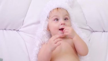 Beyaz yumuşak şapkalı küçük çocuk beyaz kanepeye oturur ve gülümsüyor