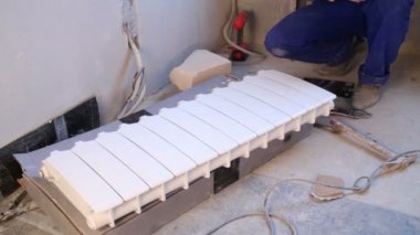 Worker assembles radiator lying on cardboard box in room
