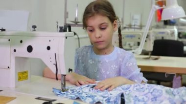Küçük kız dikiş makinesi ile masada oturur ve kumaş görünüyor
