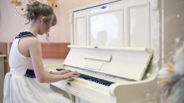 Işık odasında beyaz piyano çalan beyaz elbiseli kızın arkası