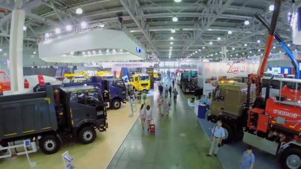 Люди ходять по павільйону з будівельними машинами під час виставки — стокове відео