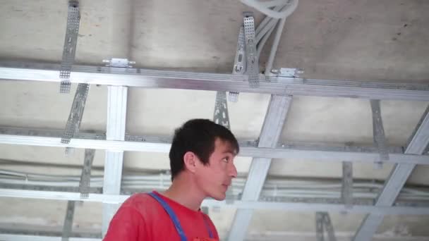 Человек в униформе устанавливает каркас для подвесного потолка с помощью отвертки — стоковое видео