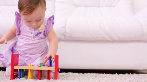 Little kid in dress plays with wooden toy on carpet near sofa — Stock Video