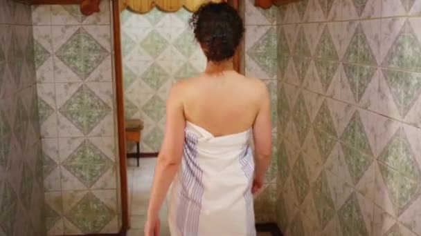 Parte posterior de la mujer joven envuelta en sábanas que entran en la sauna espaciosa — Vídeos de Stock