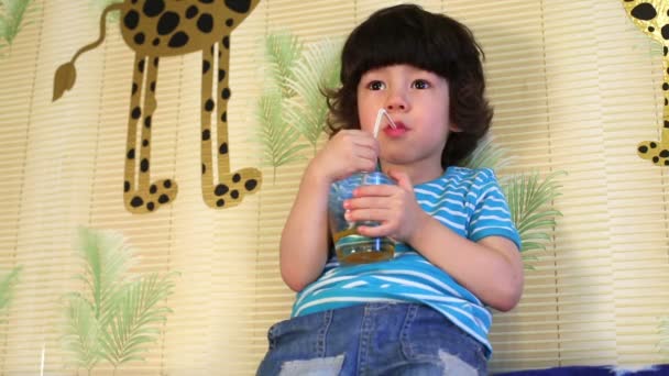 Little boy sits on back of sofa leaning at wall and drinks — Stock Video