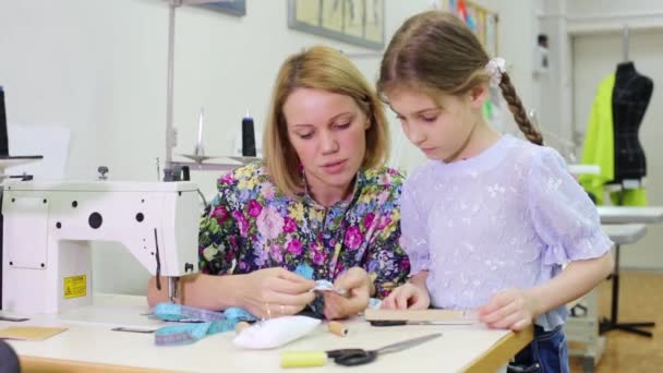 Vrouwelijke kleermaker zit aan tafel en leert meisje hoe werk — Stockvideo