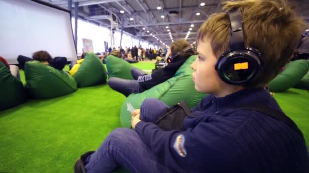 Boy in headphones looks at big screen at conference — Stock Video