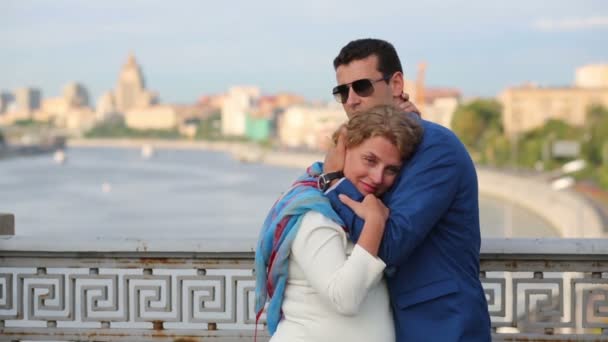 Hübsche Frau in Weiß und junger Mann umarmen sich auf Brücke — Stockvideo