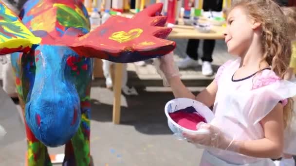 Linda niña en pinturas de color rosa alce de madera al aire libre en el día de verano — Vídeos de Stock